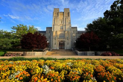 Burruss Hall in May with a clear sky and flowers in front of the building.